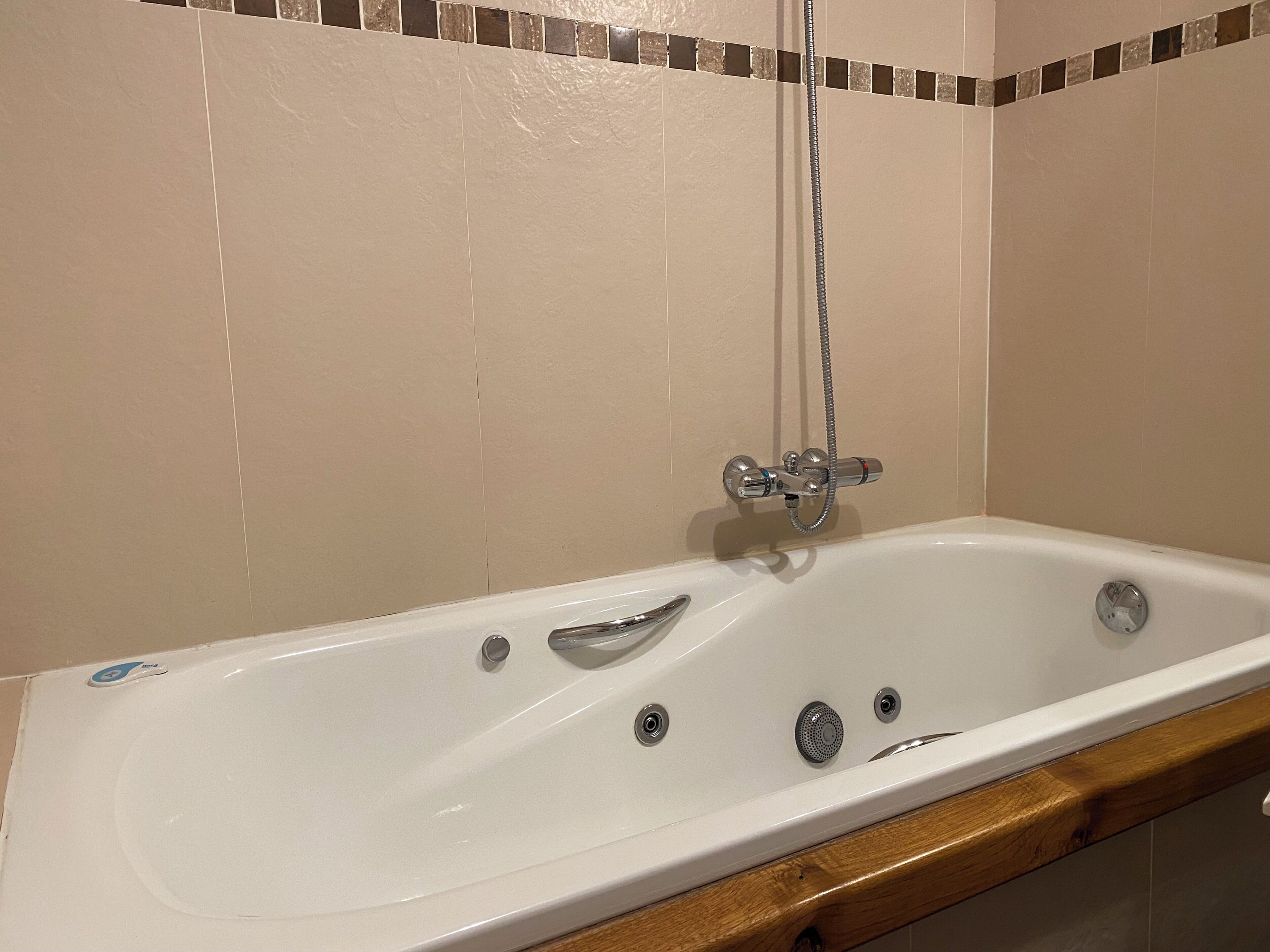 A white bathtub with a shower head, a faucet, and a drain.