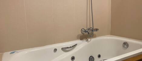 A white bathtub with a shower head, a faucet, and a drain.