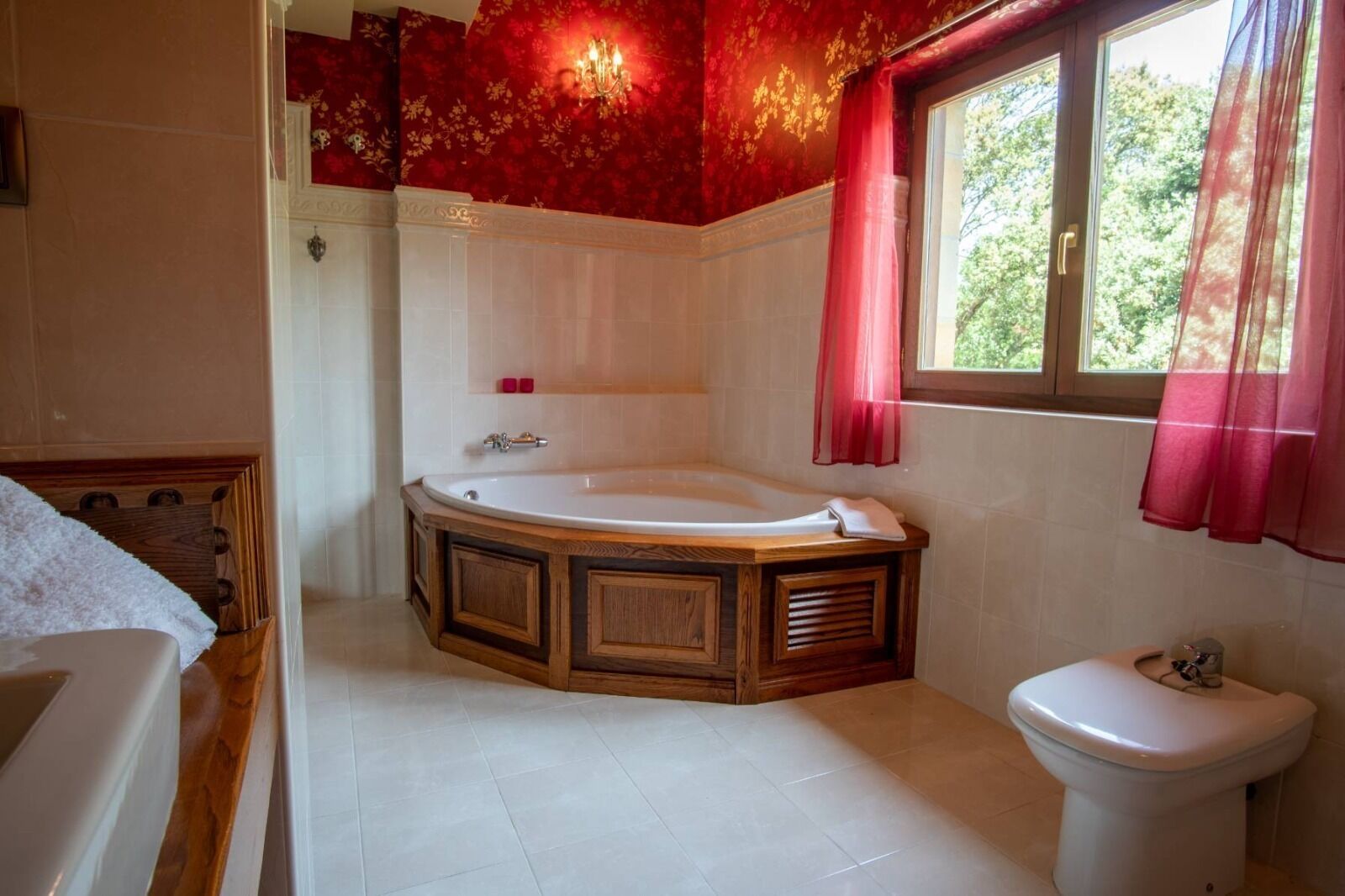 A bathroom with a freestanding bathtub, a toilet, and a window with red curtains.