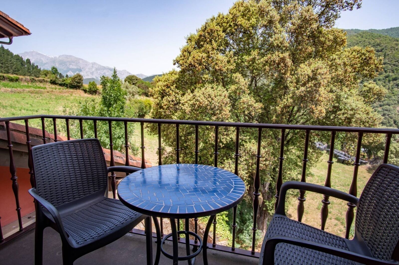 A balcony with a table and two chairs, overlooking a mountainous landscape.