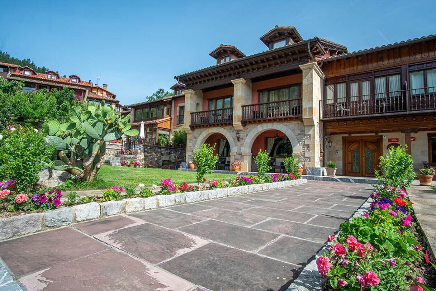 Un hotel con fachada de piedra, varios balcones y un jardín cuidado con plantas florecientes.