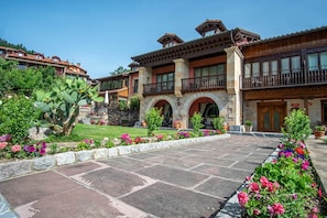 A hotel with a stone facade, multiple balconies, and a well-maintained garden with flowering plants. - Hotel Finca Malvasia (Cabezon de Liebana)