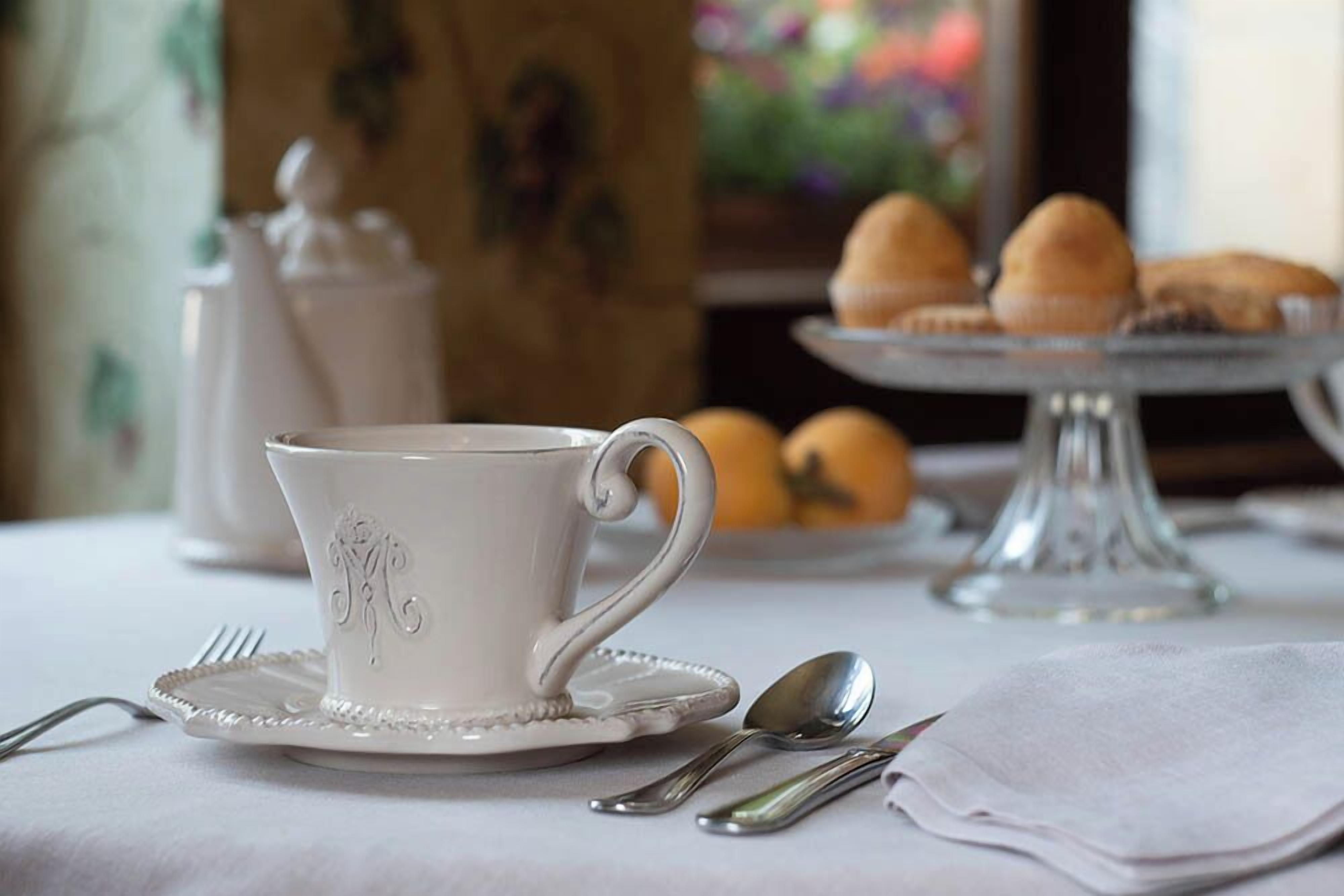 A white cup with a handle on a saucer, a plate with a fork, a spoon, and a napkin on a table.