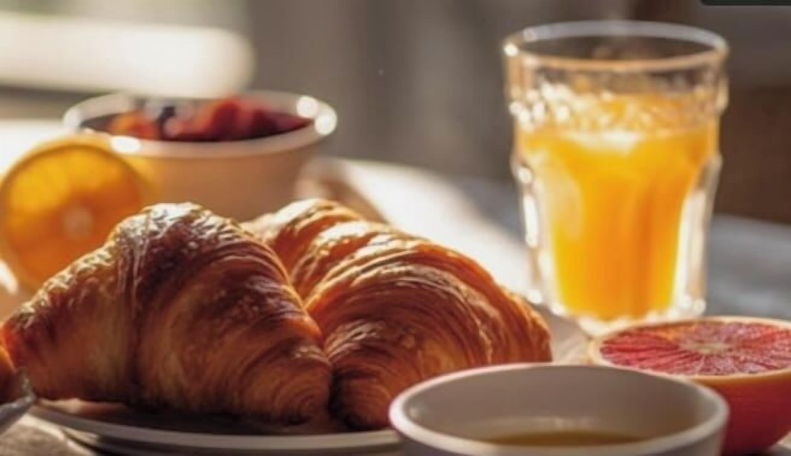 A breakfast setting with croissants, a glass of orange juice, and a bowl of fruit.