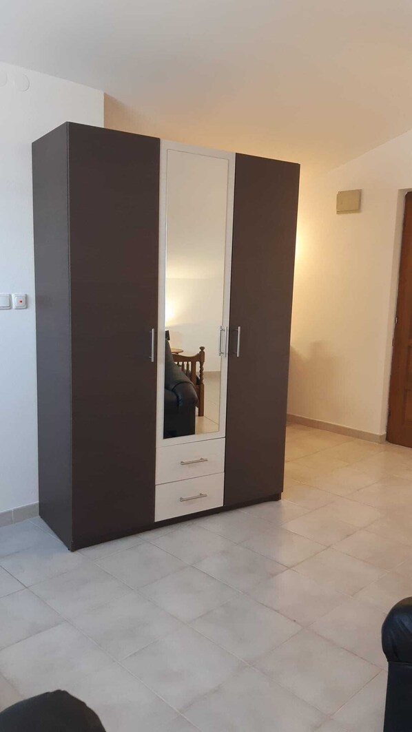 A wardrobe with a mirrored door, a small table, and a chair in the background.