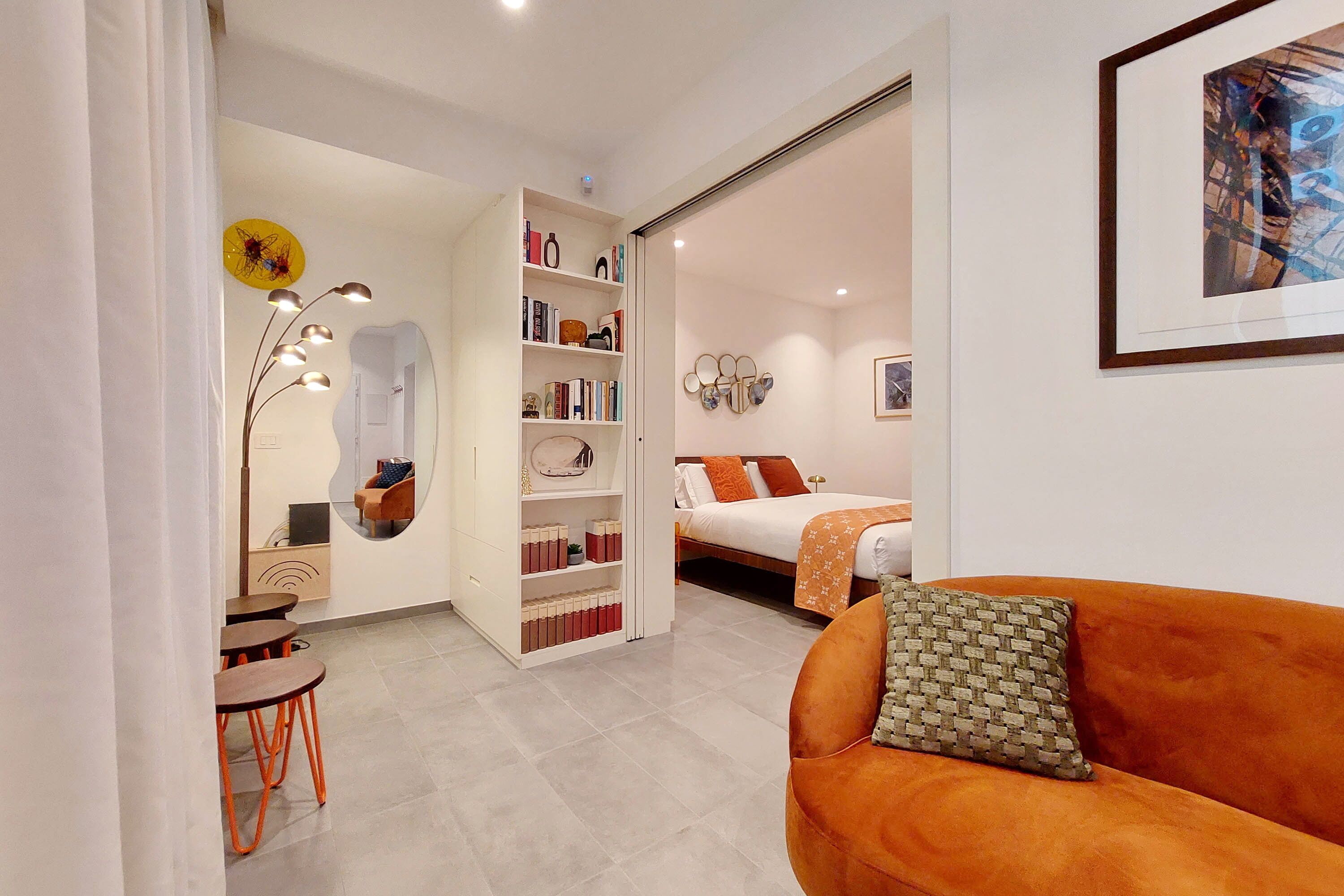 A modern bedroom with a bed, a sofa, a bookshelf, and a desk with chairs.