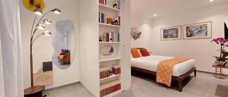 A modern bedroom with a bed, a bookshelf, a mirror, and a small table with a plant.