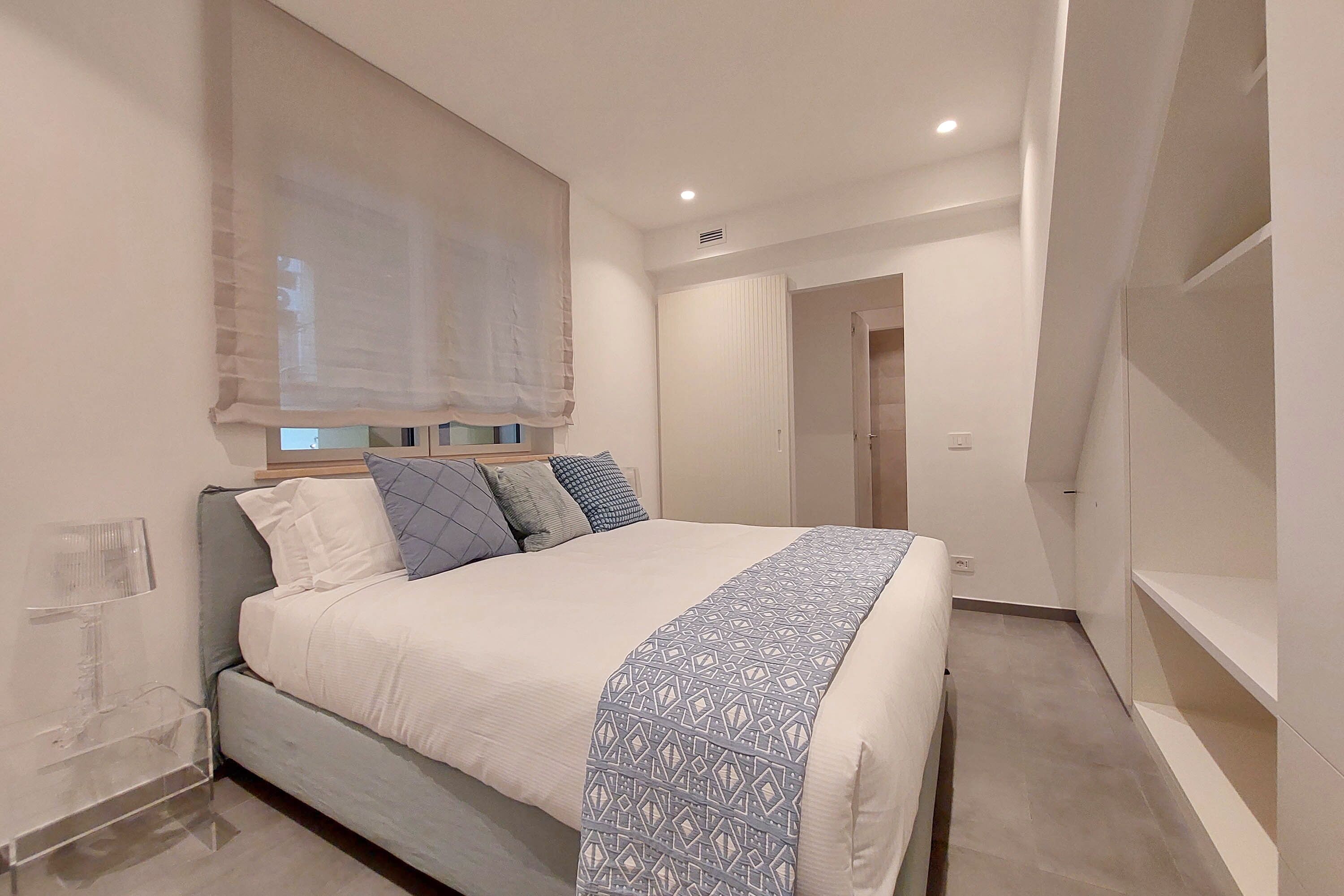 Une chambre moderne avec un grand lit, une table de chevet et une fenêtre ornée de rideaux légers.