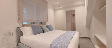 Une chambre moderne avec un grand lit, une table de chevet et une fenêtre ornée de rideaux légers.