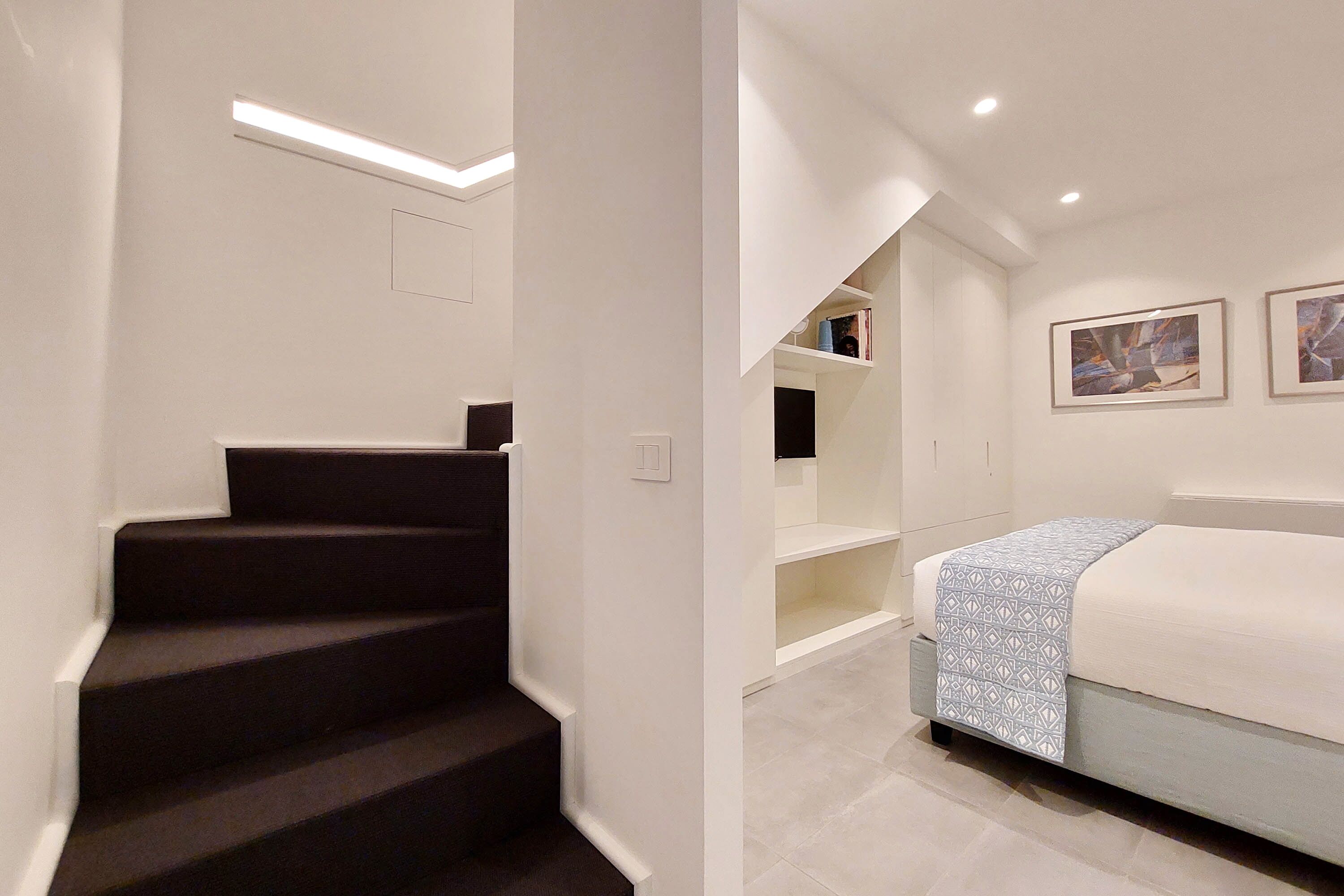 Un dormitorio moderno con cama, mesita de noche y una escalera que sube a una zona superior.