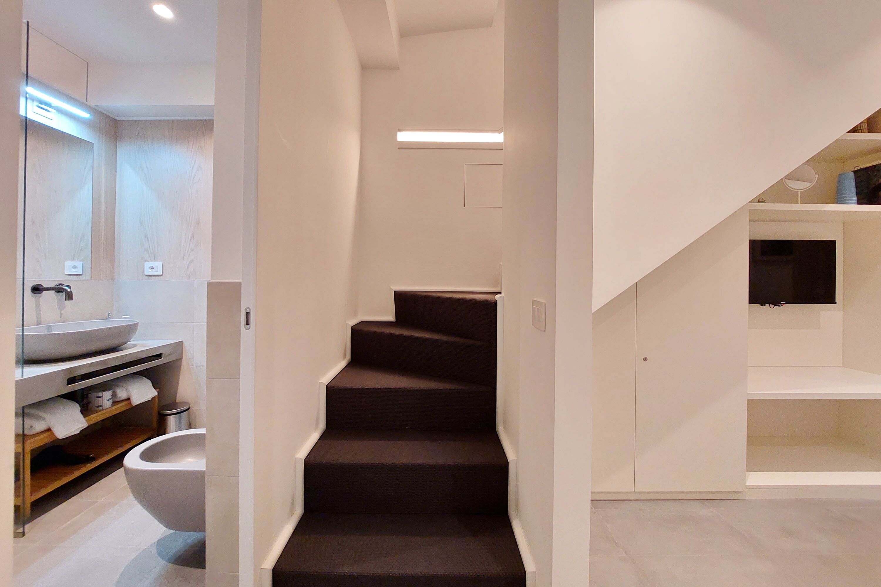A modern bathroom with a large sink, toilet, and a staircase leading to another room.