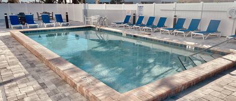 A rectangular swimming pool with a tiled edge, surrounded by lounge chairs and a white fence.