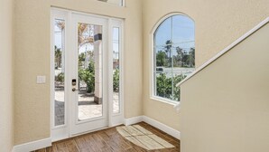 A hallway with a double door leading to an outdoor area, a large arched window, and a wooden floor. - 3134 Estero Blvd 5 Bedroom Home by RedAwning (Fort Myers Beach)