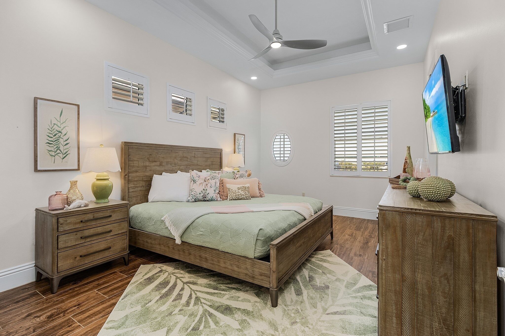 A bedroom with a bed, nightstands, a dresser, a ceiling fan, and a TV mounted on the wall.