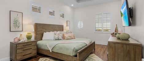 A bedroom with a bed, nightstands, a dresser, a ceiling fan, and a TV mounted on the wall.