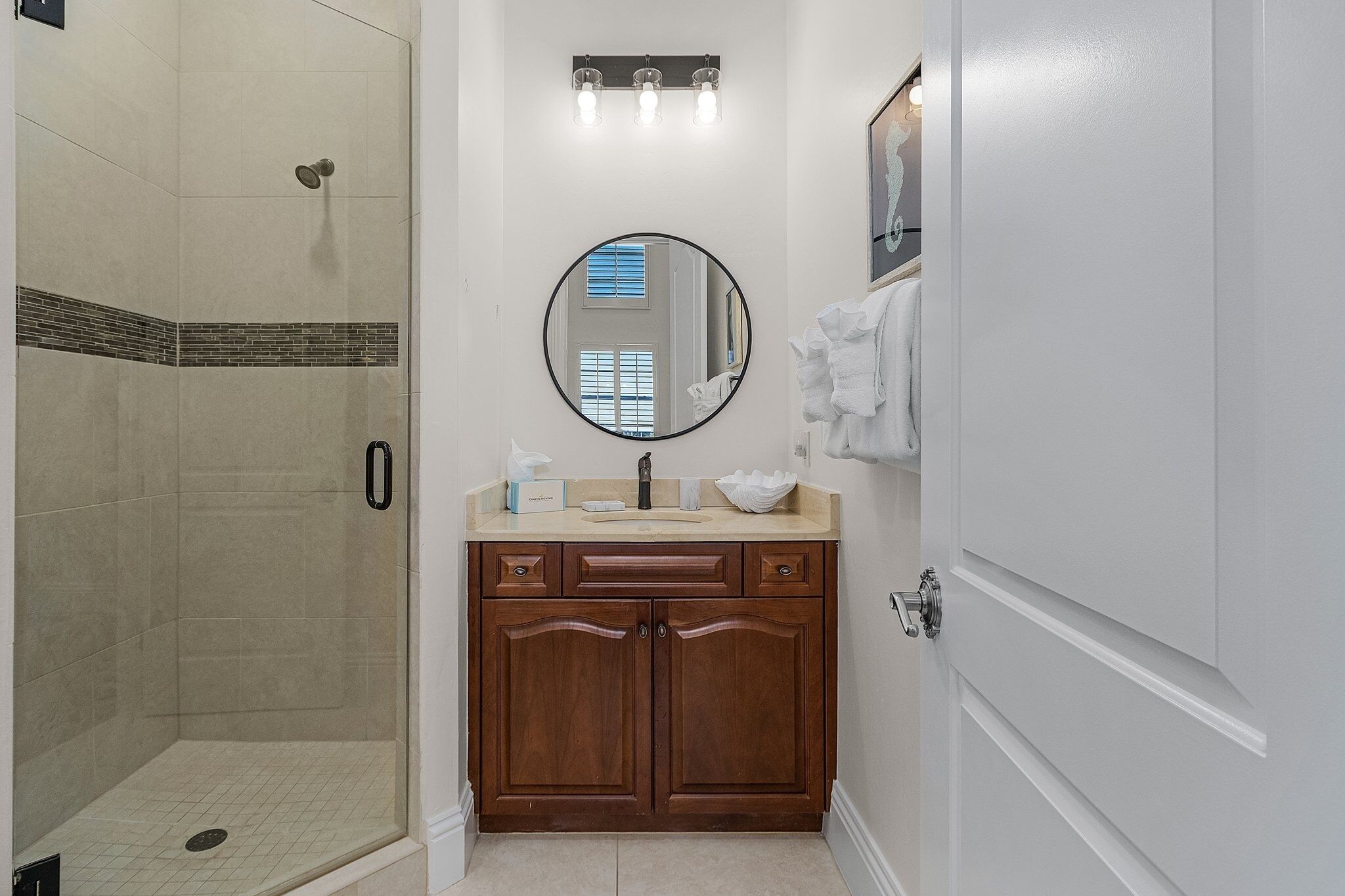 A bathroom with a walk-in shower, a round mirror, a sink with a vanity, and a towel rack.