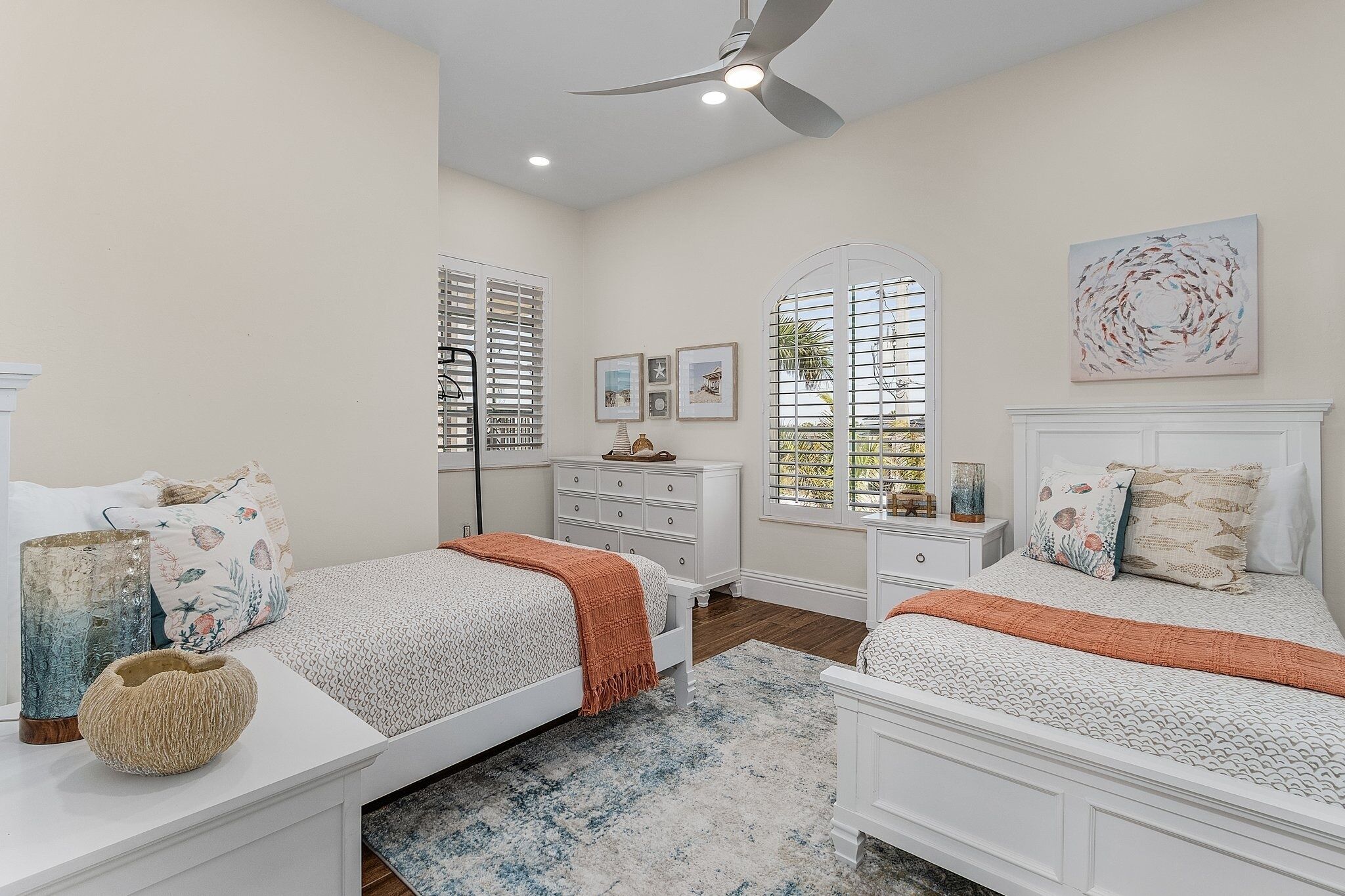 A bedroom with two beds, a ceiling fan, and a window with shutters.
