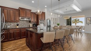 A modern kitchen with dark wood cabinets, a large island with bar stools, and pendant lighting. - 3132 Estero Blvd 5 Bedroom Home by RedAwning (Fort Myers Beach)