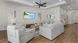 A spacious living room with a ceiling fan, a large flat-screen TV, and a dining area with a wooden table and chairs. - 3132 Estero Blvd 5 Bedroom Home by RedAwning (Fort Myers Beach)
