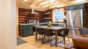 Une cuisine moderne avec des poutres en bois, un réfrigérateur en acier inoxydable et un coin repas comprenant une table et des chaises.