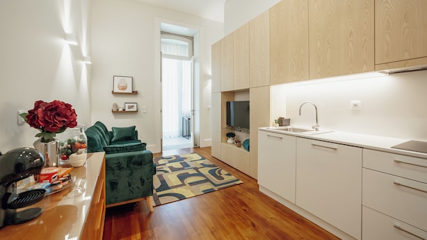 A modern kitchen with white cabinets, a built-in oven, and a sink. There is a green sofa and a coffee table in the living area. - Home with a Pool by Vacationy (Porto)