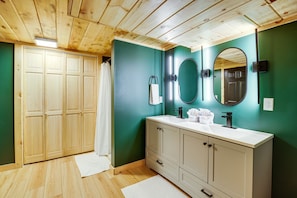 A bathroom with wooden flooring, a white vanity, a mirror, and a green wall. - Secluded Naples Cabin w/ Deck & Stream Views (Naples)