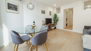 Ein modernes Wohnzimmer mit einem Glastisch, grau gepolsterten Sesseln, einem Flachbildfernseher und einer Topfpflanze.
