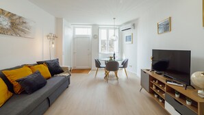 Ein modernes Wohnzimmer mit grauem Sofa, gelben Kissen, einem Glastisch und einem Flachbildfernseher.