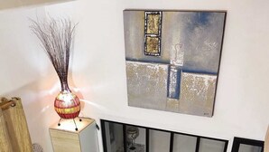Een moderne woonkamer met een grijze bank, een decoratieve lamp, een schilderij en een raam met jaloezieën.