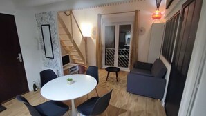 Een gezellige woonkamer met een ronde tafel, twee stoelen, een bank, een trap en een schuifdeur naar een andere kamer.