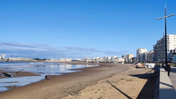 Een strand met een zandstrand, een steiger en gebouwen op de achtergrond.