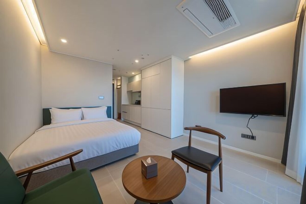 Una habitación de hotel moderna con una cama, un televisor montado en la pared, una mesita y una silla.