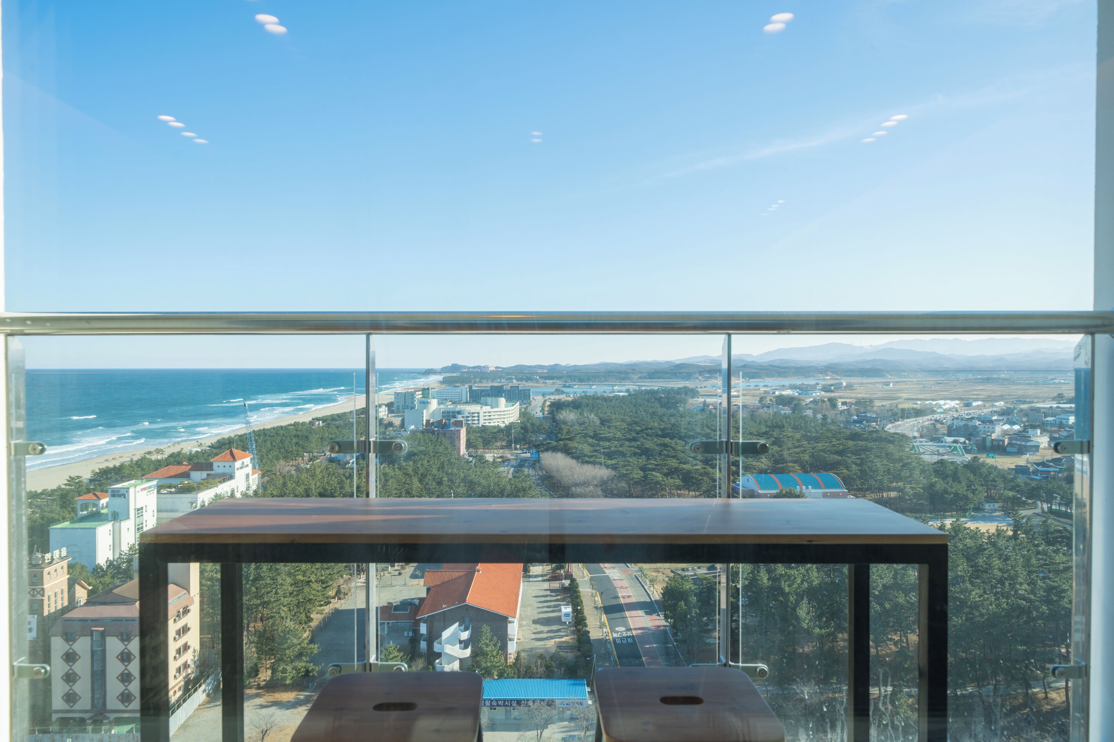 Una habitación con un ventanal que ofrece vistas a un paisaje urbano costero, incluyendo una playa y edificios.