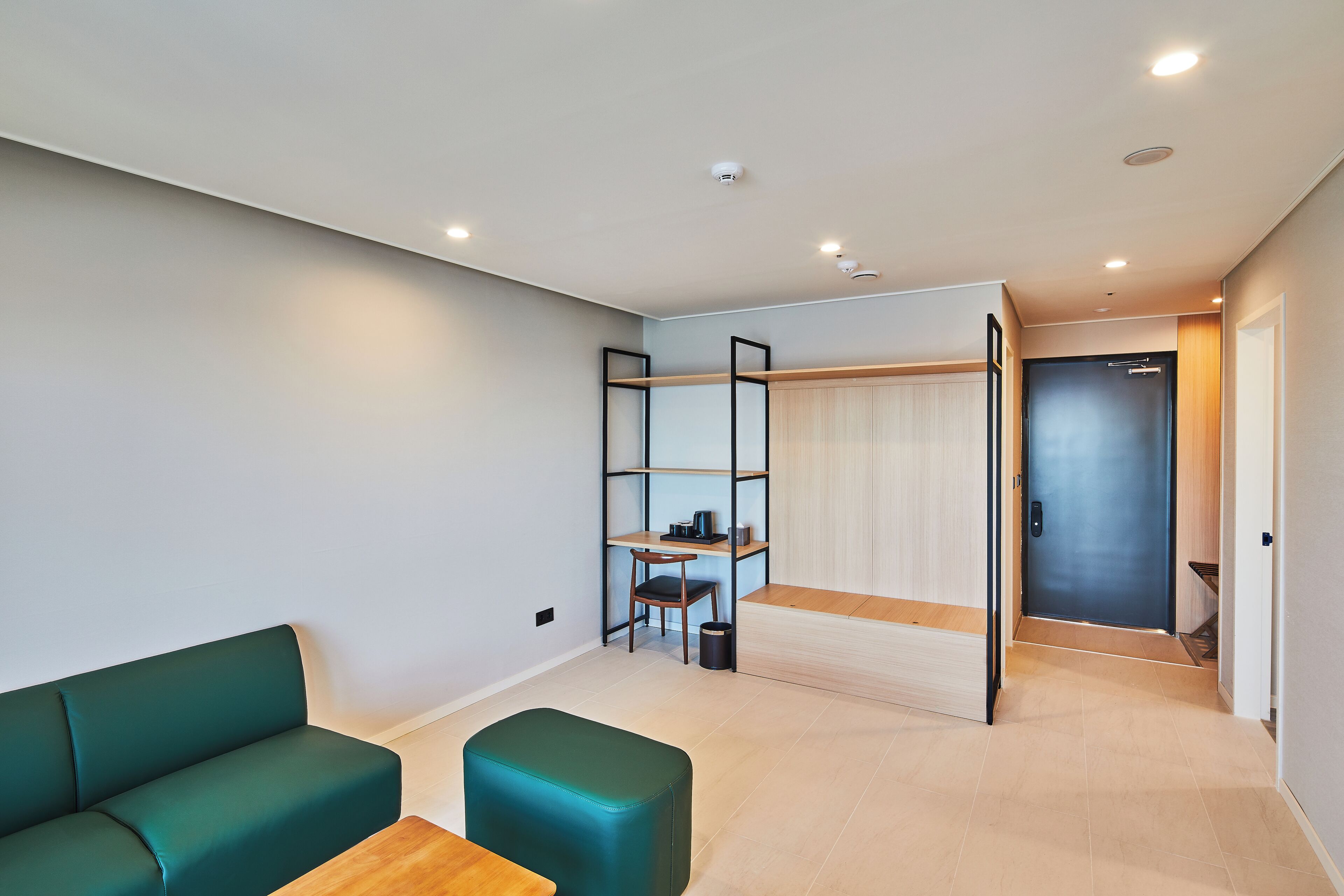 A modern room with a sofa, a small table, a desk with a chair, and a wardrobe.