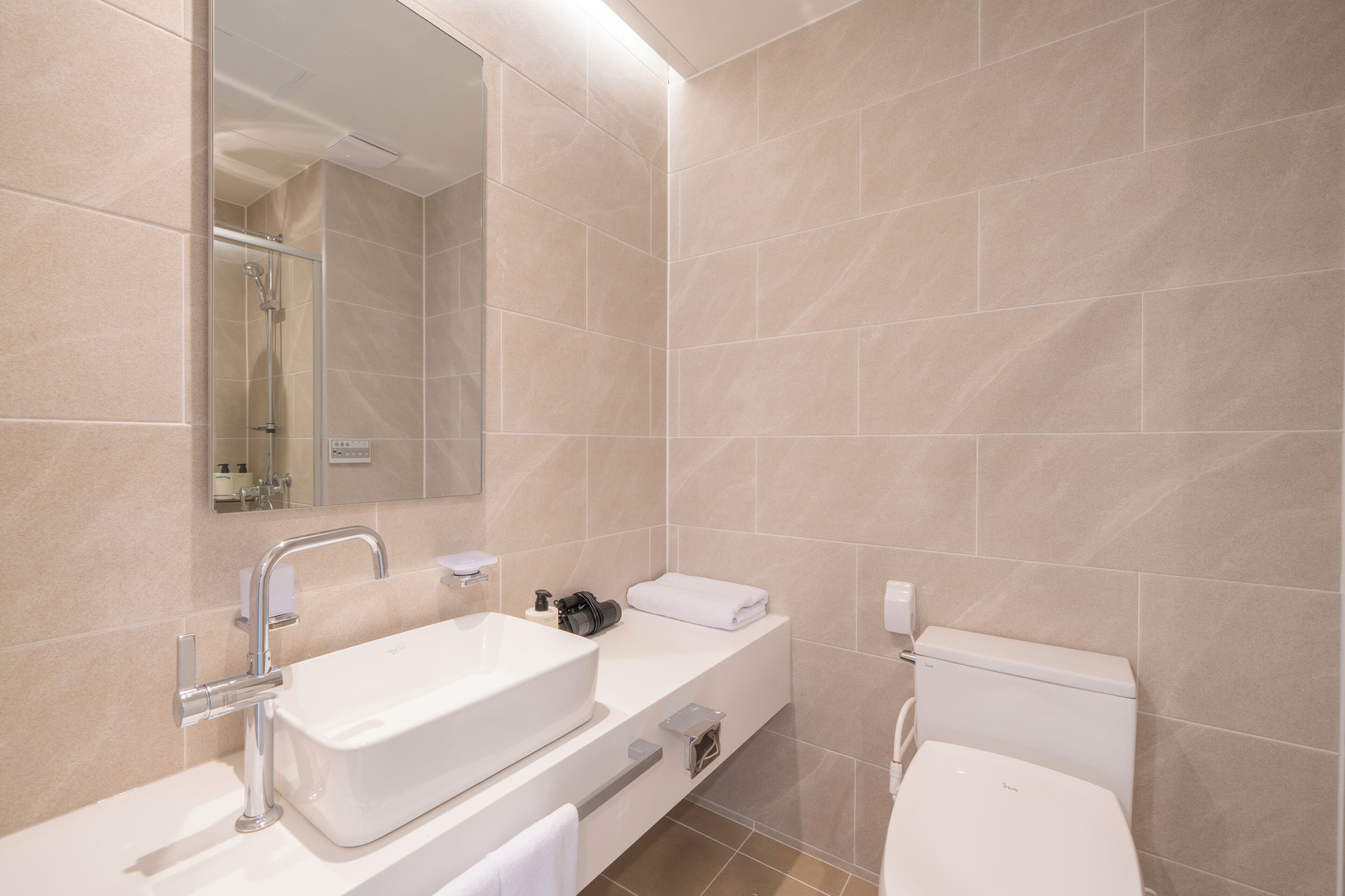 A modern bathroom with a large mirror, a white sink, a toilet, and a shower area.