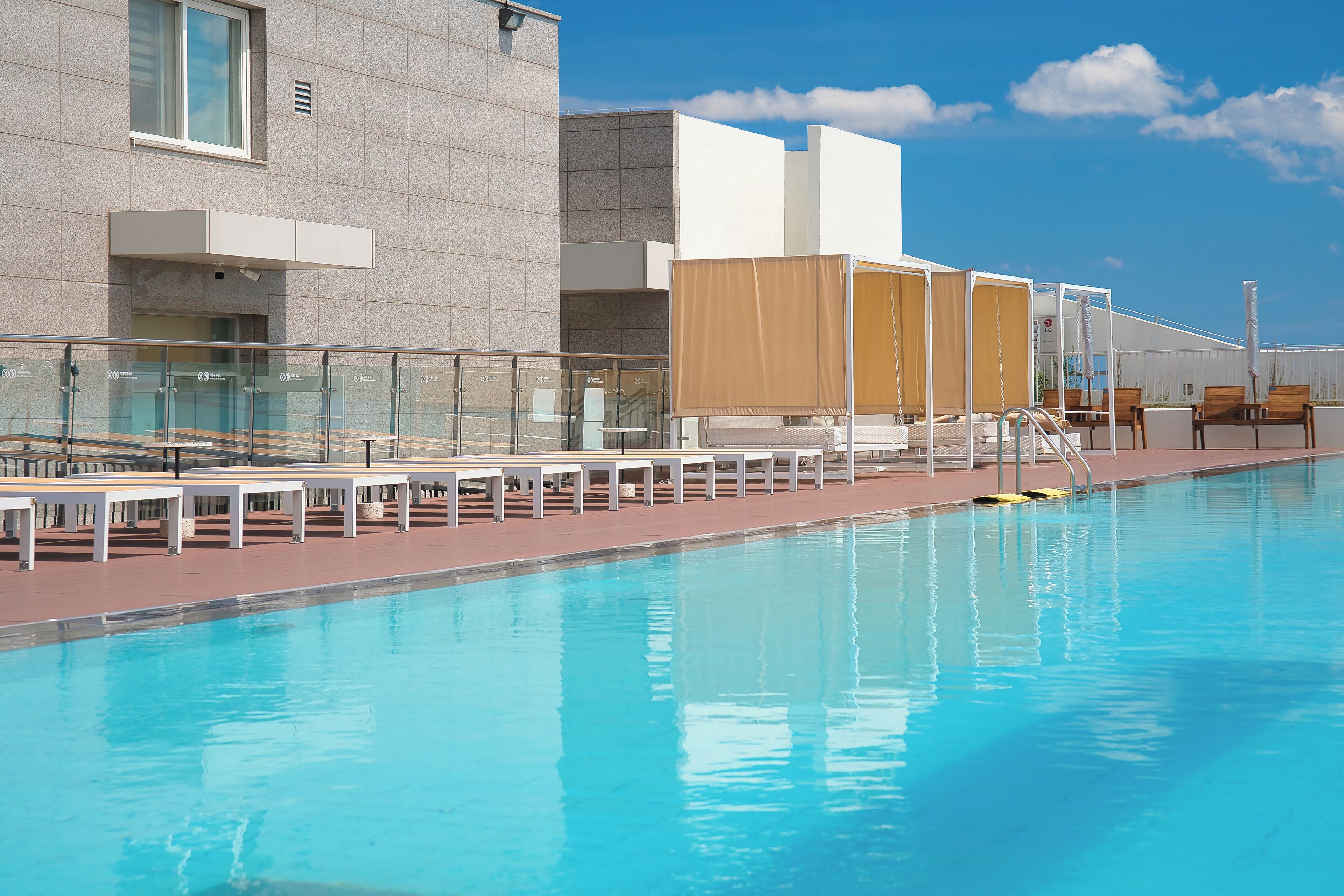 A swimming pool with sun loungers and a glass railing, adjacent to a building with a modern design.