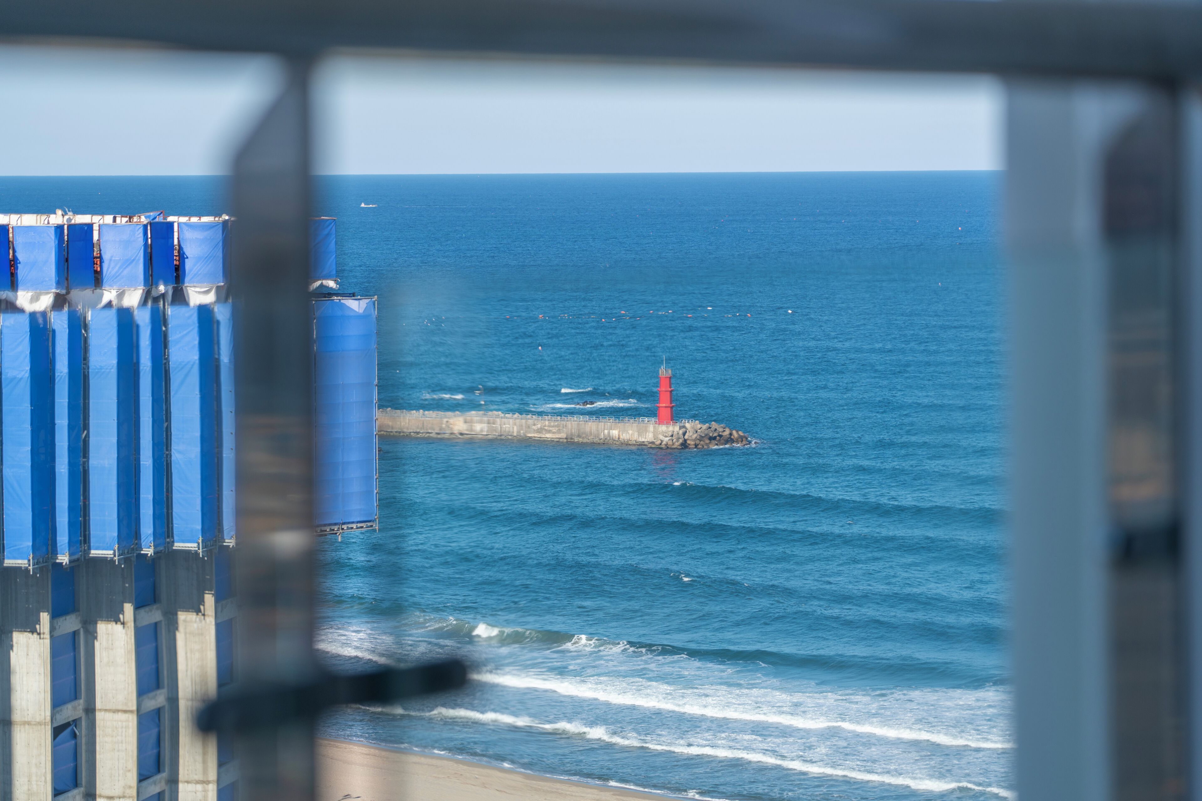 A coastal view with a lighthouse, ocean, and a pier with blue structures.