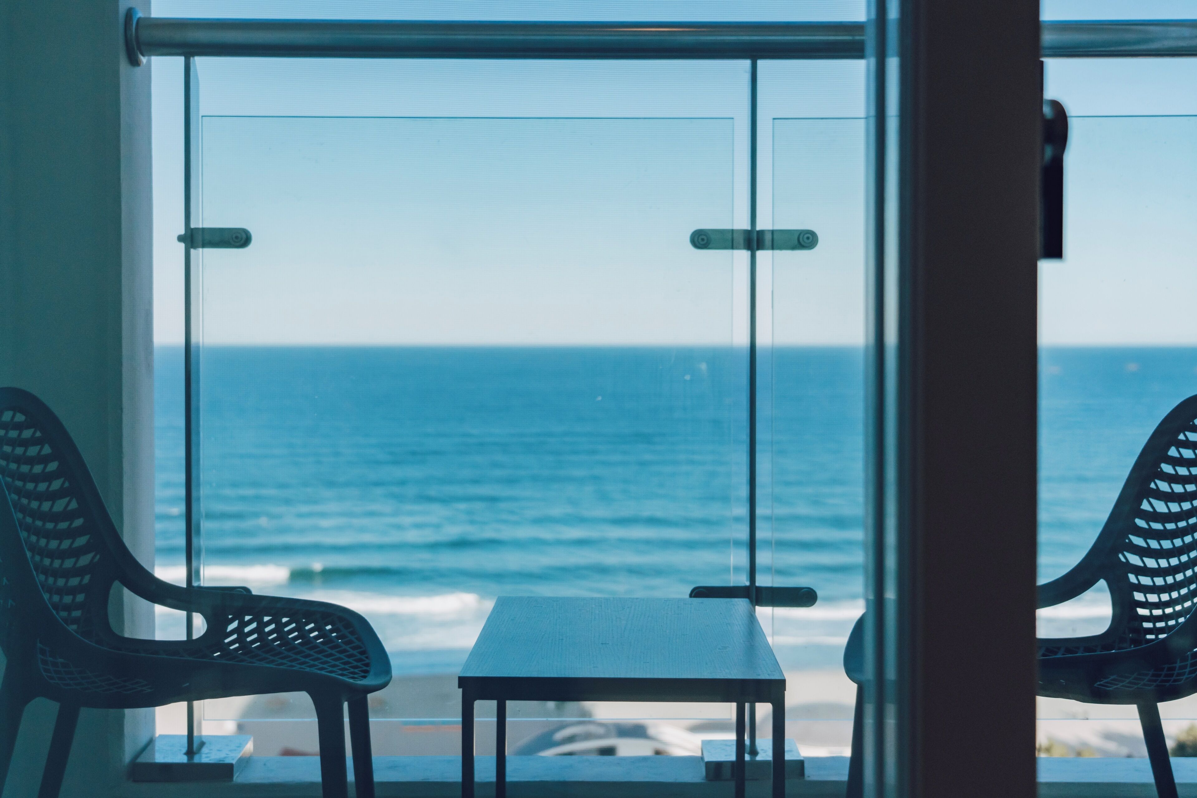 A room with a view of the ocean, a table, and two chairs.