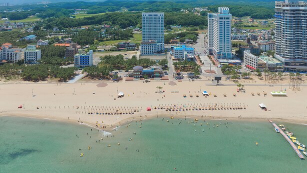 Paesaggio costiero con edifici moderni, una spiaggia sabbiosa e cielo sereno.