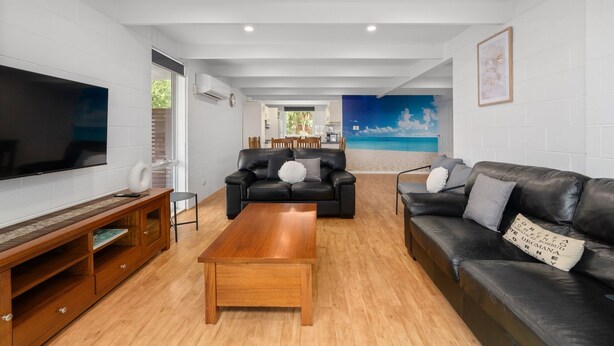 Ein modernes Wohnzimmer mit Flachbildfernseher, Ledersofas, einem Holztisch und einer Wandmalerei mit Strandmotiv.