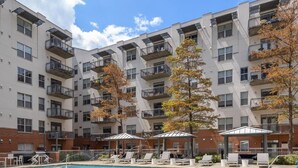 A swimming pool with lounge chairs and umbrellas, surrounded by multi-story buildings with balconies. - Austin Exclusive 1BD 1BA Downtown Apartment (Austin)