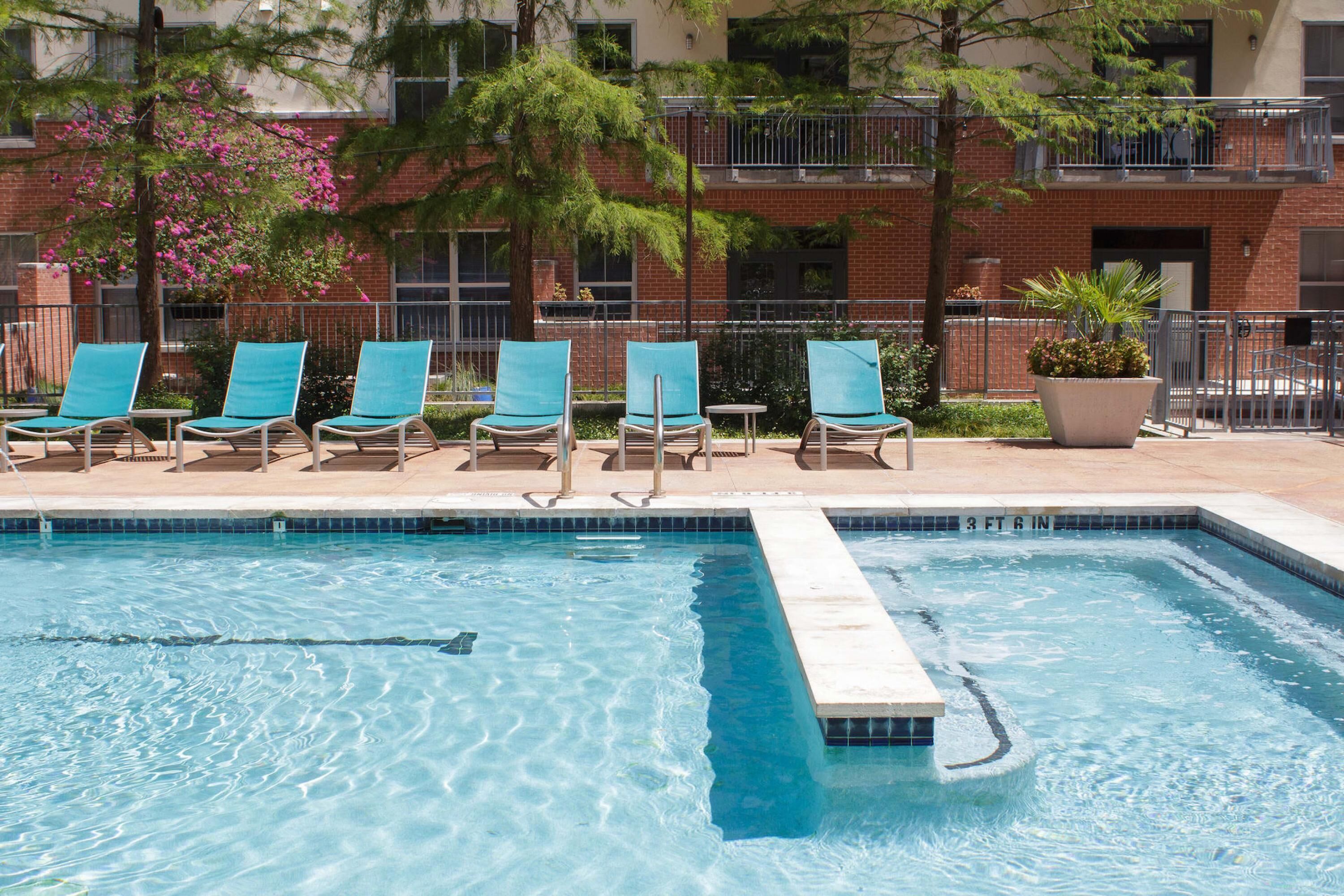 A swimming pool with lounge chairs and a brick building in the background.