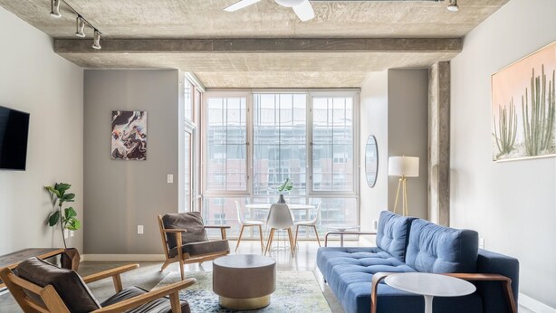 A modern living room with a blue sofa, wooden chairs, a round ottoman, and a small table.