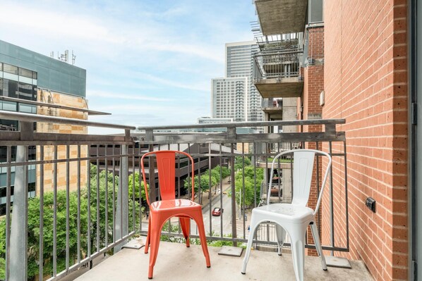 A balcony with two chairs, a view of a cityscape, and a brick building.