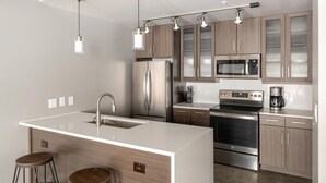 A modern kitchen with stainless steel appliances, wooden cabinets, and pendant lighting.