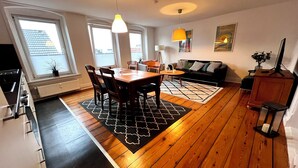 A modern living space with a dining area, kitchen, and seating area. - Ferienwohnung Apartment No. 9 in Husum für bis zu 2 Personen (Husum)