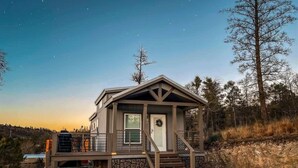 A small, single-story cabin with a porch, a door with a wreath, and a stone foundation. - Bear Hug Cabin (Ruidoso Downs)