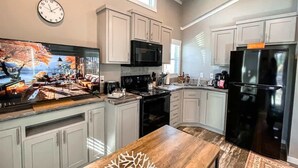 A modern kitchen with white cabinets, a black refrigerator, a microwave, and a large window. - Bear Hug Cabin (Ruidoso Downs)