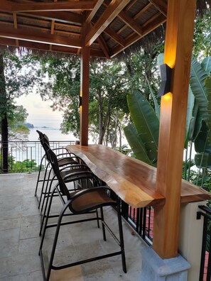 Ein Holztisch mit Stühlen unter einer Holzpergola, mit Blick auf ein Gewässer.