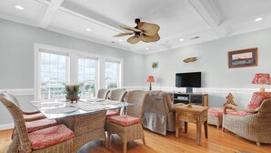 A spacious living room with a high ceiling, a ceiling fan, a flat-screen TV, a fireplace, and a dining area with wicker furniture. - Do you want to go to the beach "Oar Knot"? (Carolina Beach)